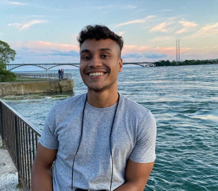 Photo of Keenan McKenley smiling and standing on Buffalo's Bird Island Pier with water and Peace Bridge in background