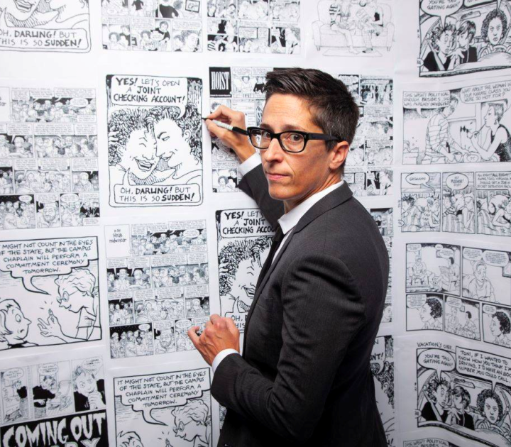 Cartoonist Alison Bechdel poised with marker in front of a wall of comics