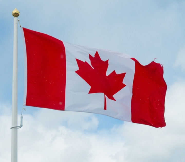 Canadian flag waving in the breeze on a flagpole against a blue sky backdrop