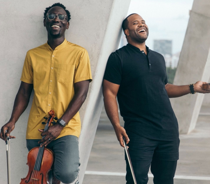Two members of Black Violin standing and smiling with their instruments