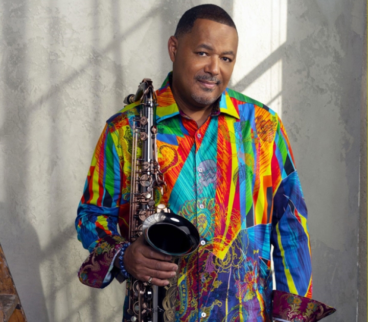 Najee in a colorful shirt holding his saxophone