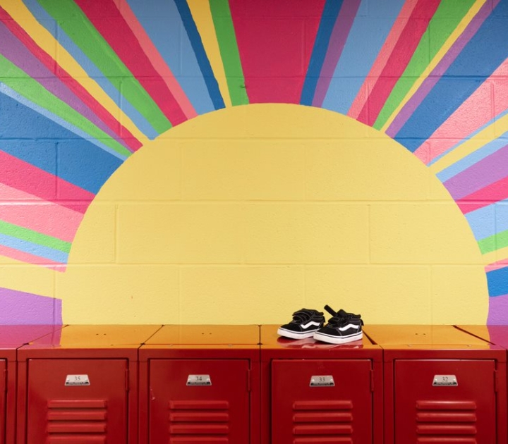 A pair of child's sneakers on top of red lockers with a sunburst mural backdrop