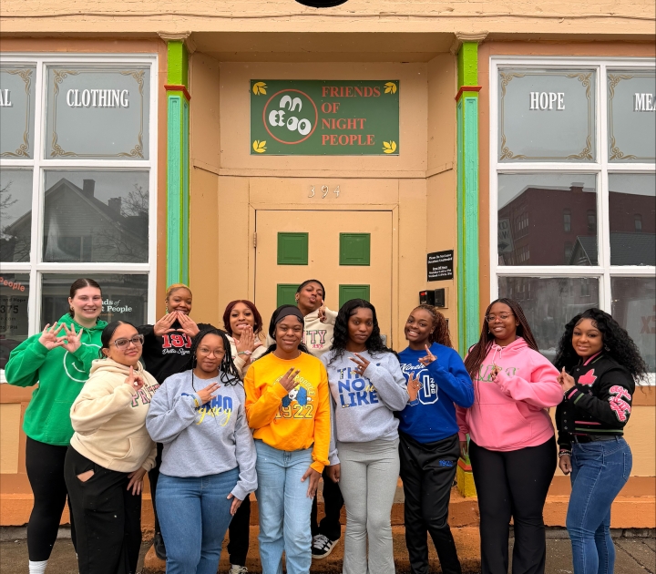 A group of female students outside a building with a sign reading Friends of Night People