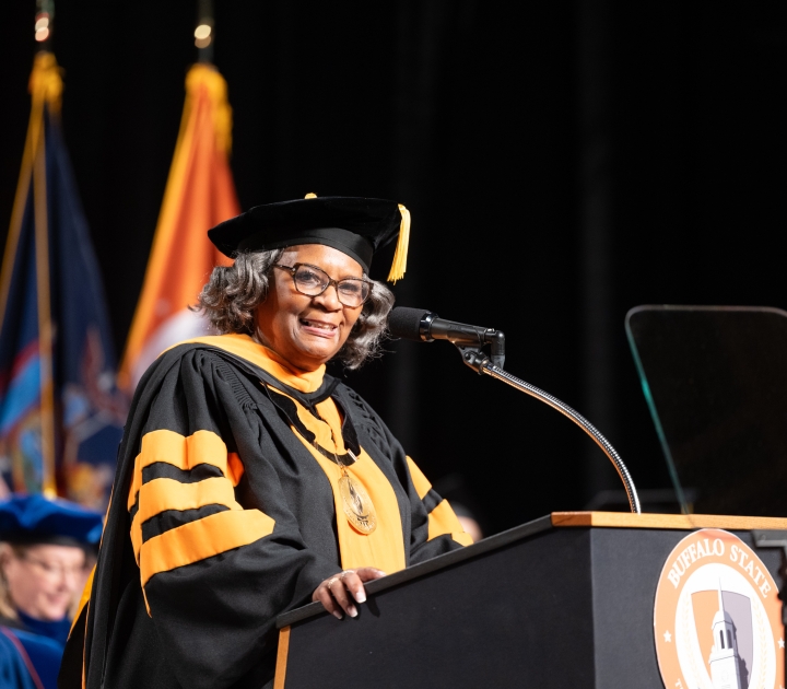 Bonita Durand stands at podium wearing regalia
