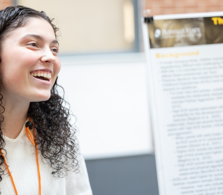 Student smiling standing in front of her research presentation poster