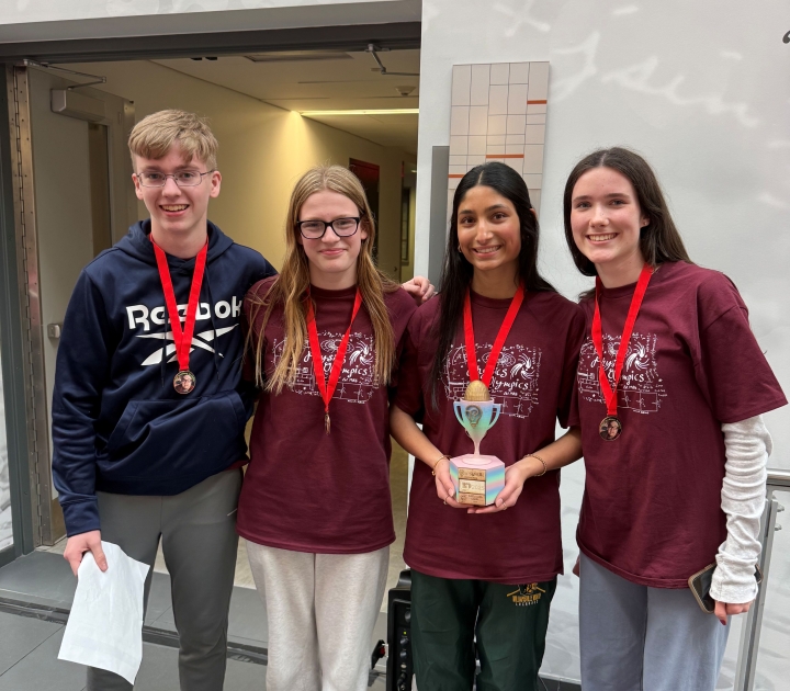 Four high school students, one holding a trophy