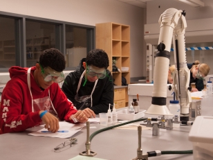 Two high school students wearing goggles and worokign together in a science lab