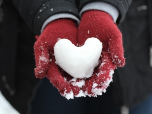 Gloved hands holding a heart-shaped snowball