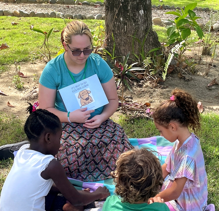 Teacher and children outside with a book.
