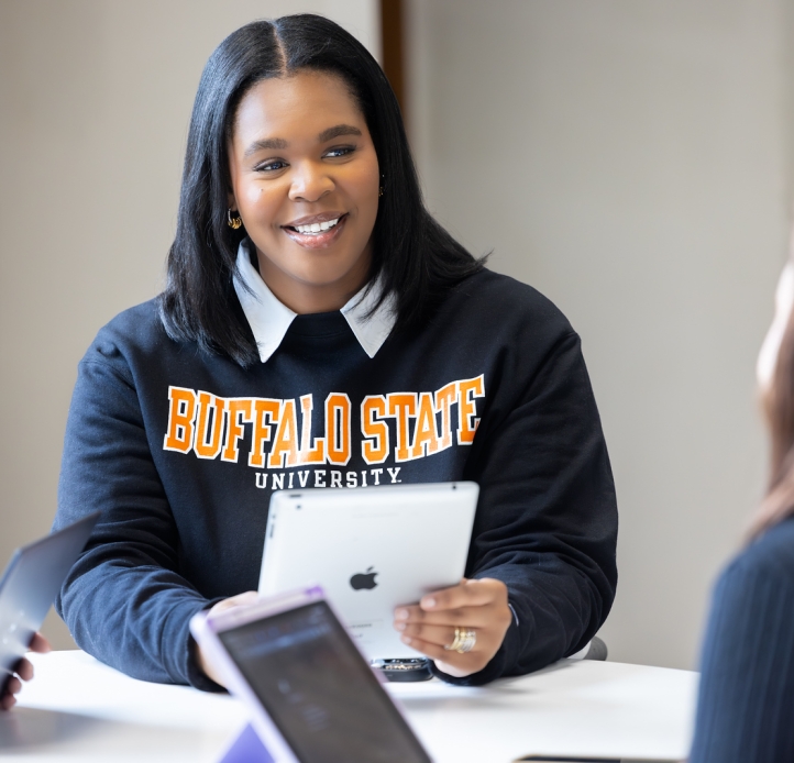 Student wearing Buffalo State University sweatshirt holds a tablet
