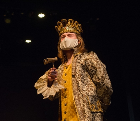 Student actor dressed in gold finery and wearing a crown