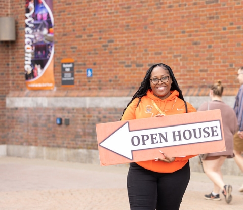 Smiling Open House tour guide holds a large sign that reads Open House with an arrow
