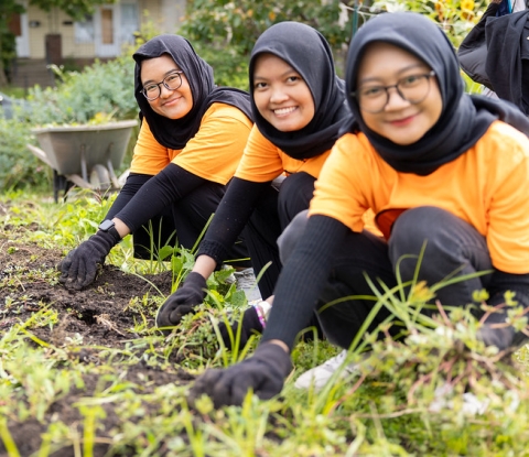 Three smiling students working in a community garden