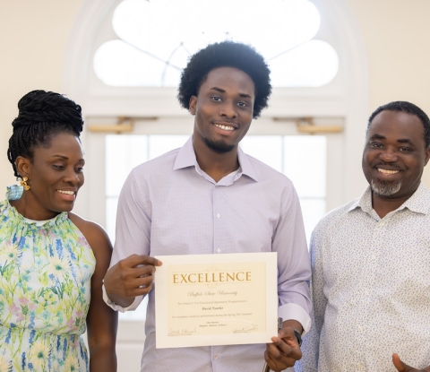 Smiling EOP honors student displaying certificate of excellence, flanked by happy family members