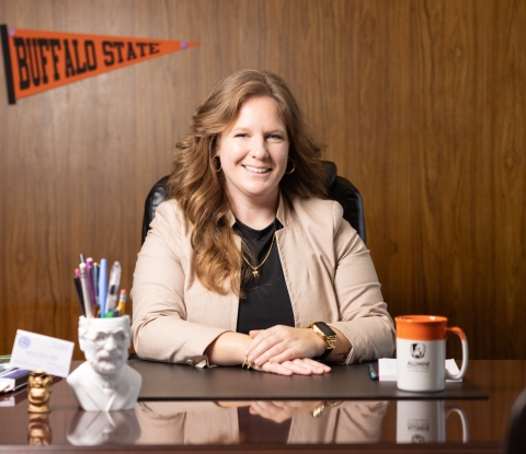 Sarah Bonk sitting at her desk with a Buffalo State pennant and mug in the background
