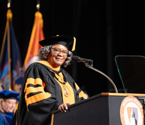 Bonita Durand stands at podium wearing regalia