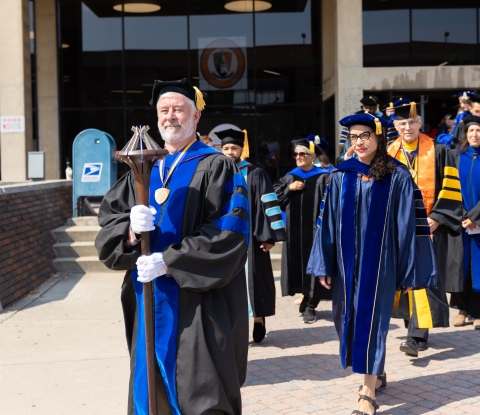 A group of faculty members process to Academic Convocation led by the mace bearer