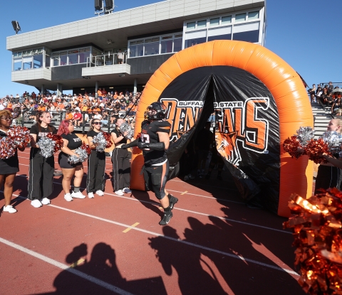 A football player bursts through a Bengal banner surrounded by cheerleaders