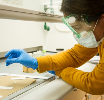 Student in goggles, gloves, and mask placing samples on a sheet