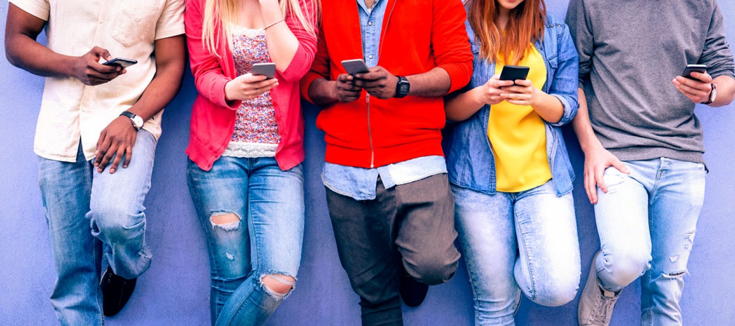 Students leaning on a wall with smart phones
