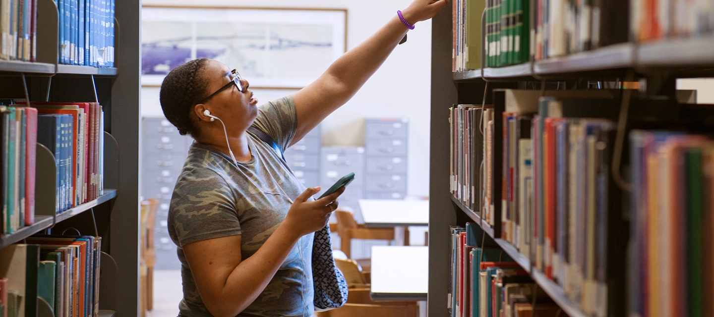 Student reaching for a book in the library stacks