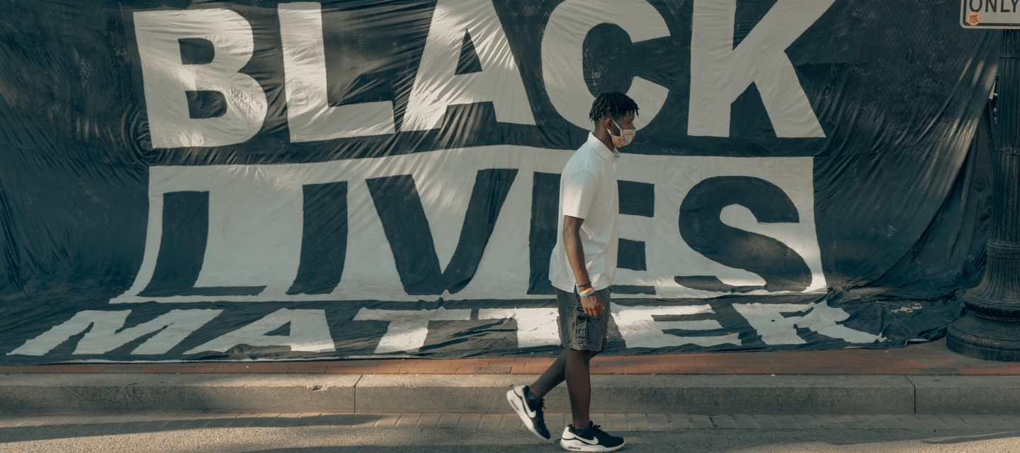 Masked male walks in front of Black Lives Matter sign