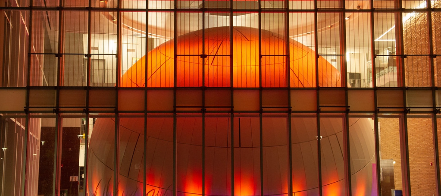 View of the planetarium lighted orange as seen from outside the Science and Math Complex
