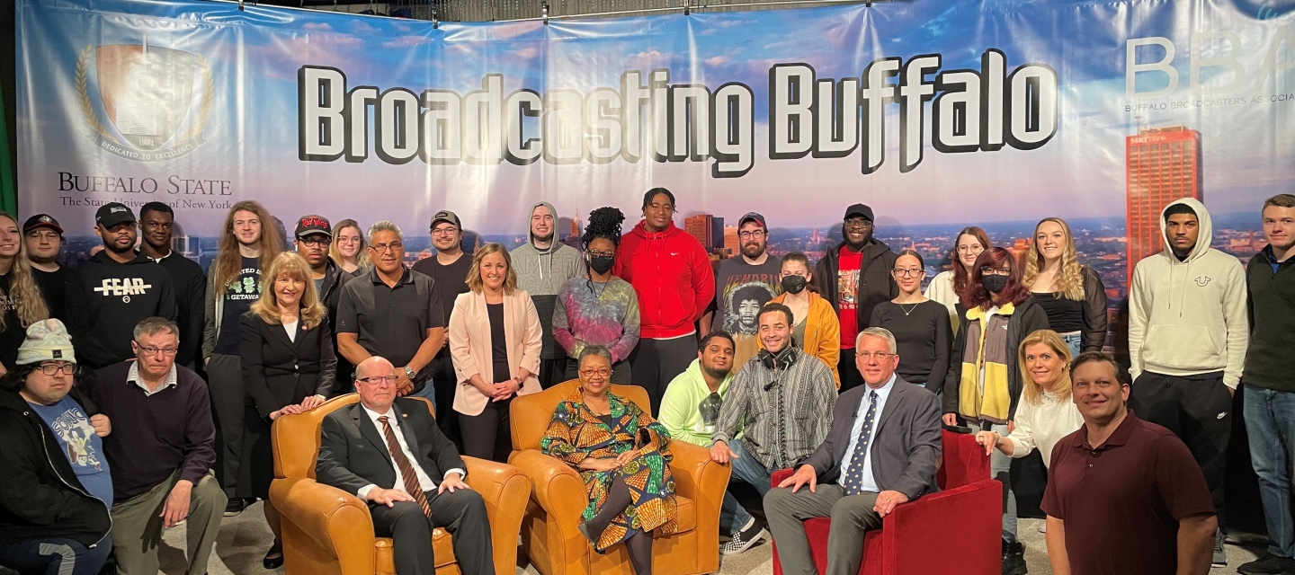 Group photo of students and faculty with President Kate Conway-Turner and Dean Brian Cronk under a banner that reads "Broadcasting Buffalo"