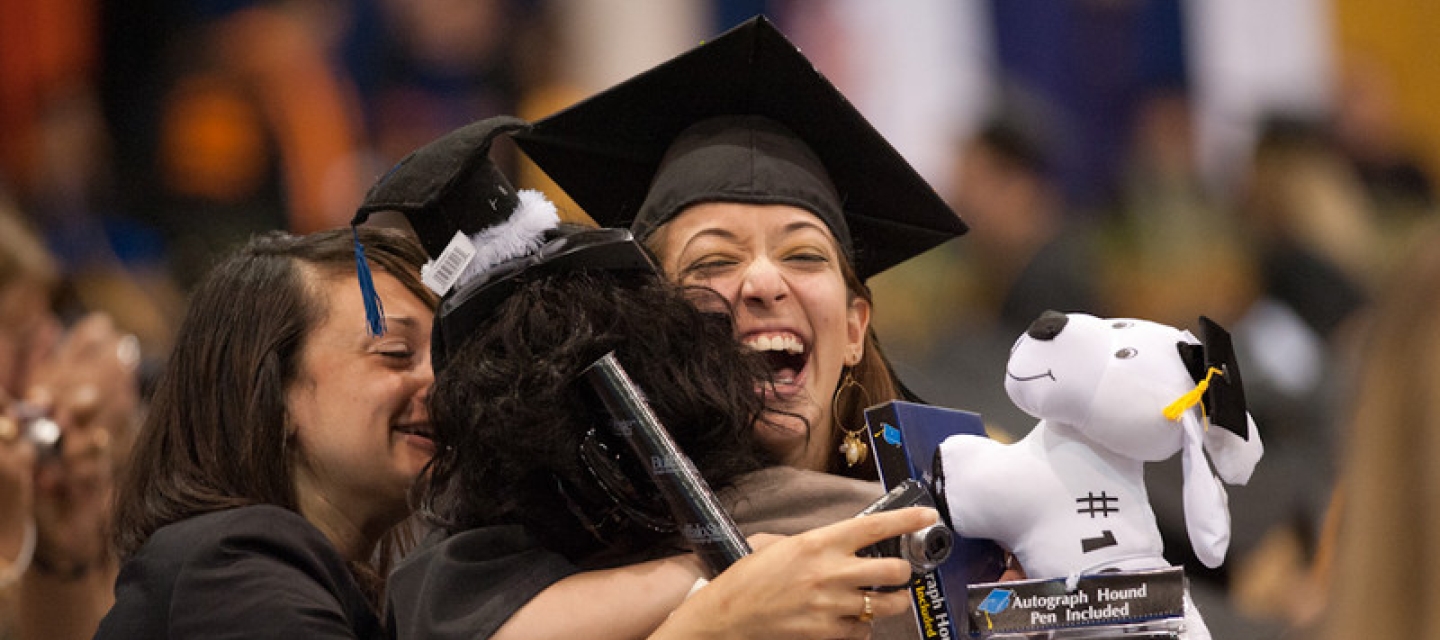 Graduating student in cap and gown jubilently hugging relative