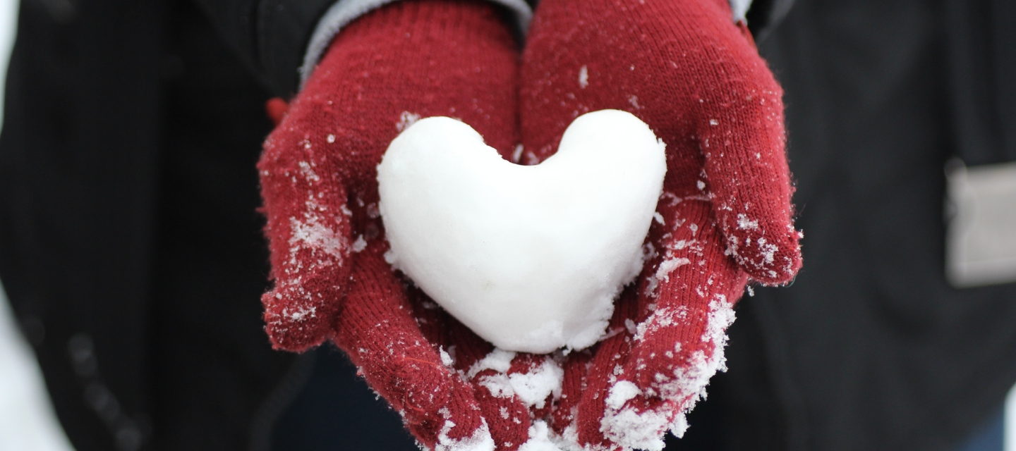 Gloved hands holding a heart-shaped snowball