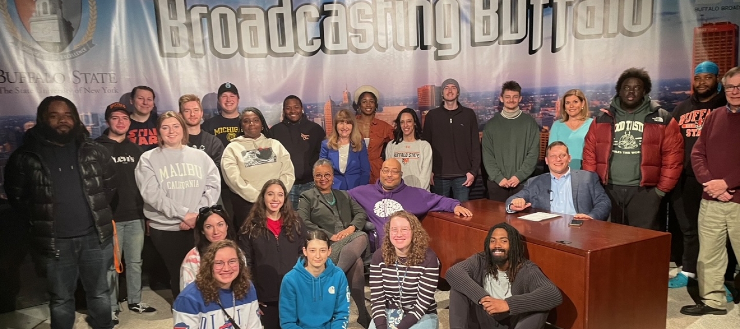 Group of students and professors in front of a sign that reads Broadcasting Buffalo
