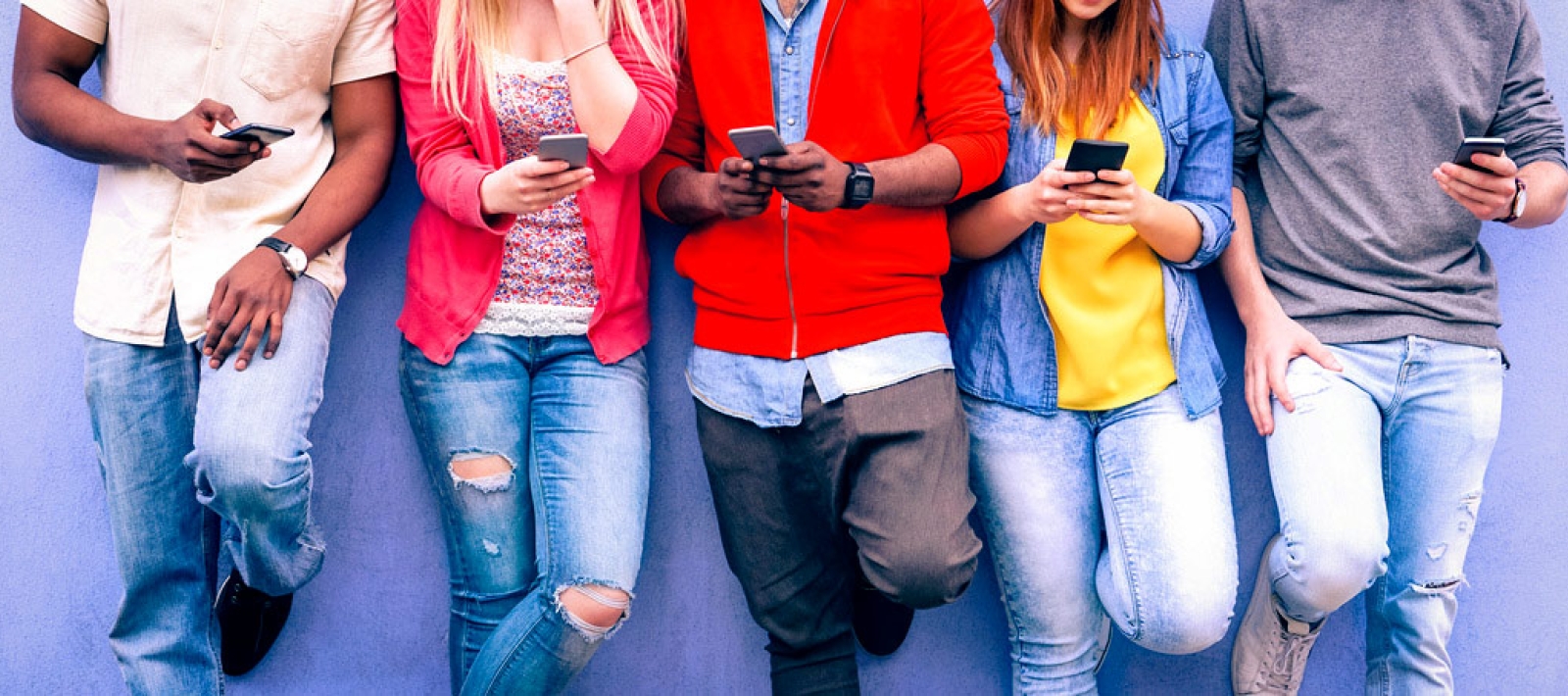 Students leaning on a wall with smart phones