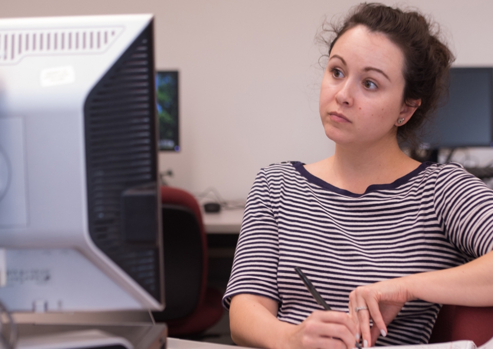 Female student taking notes in front of a computer monitor