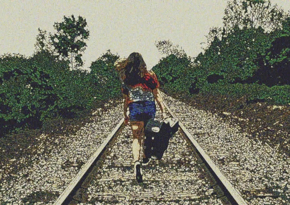 Girl walking down railroad tracks with carrying a guitar case
