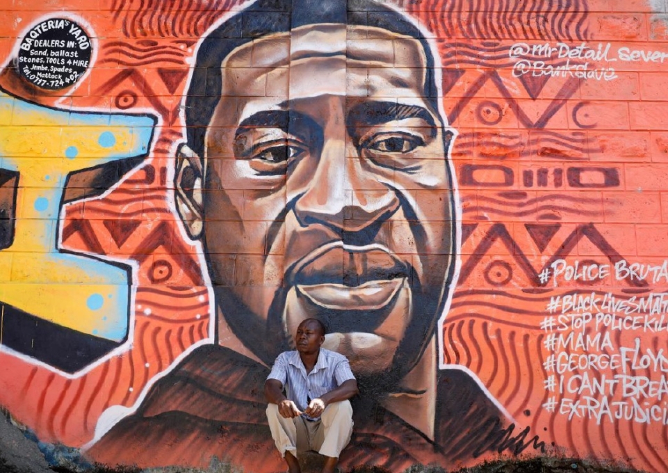 Man sitting in front of large colorful mural of George Floyd's head and shoulders