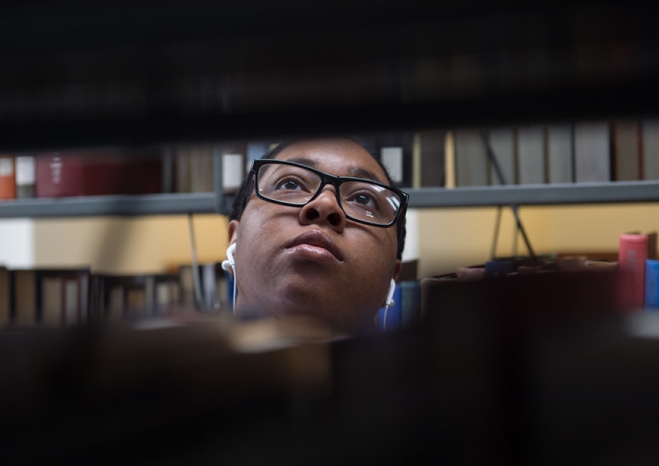 Student's face between stacks of books in the library stacks