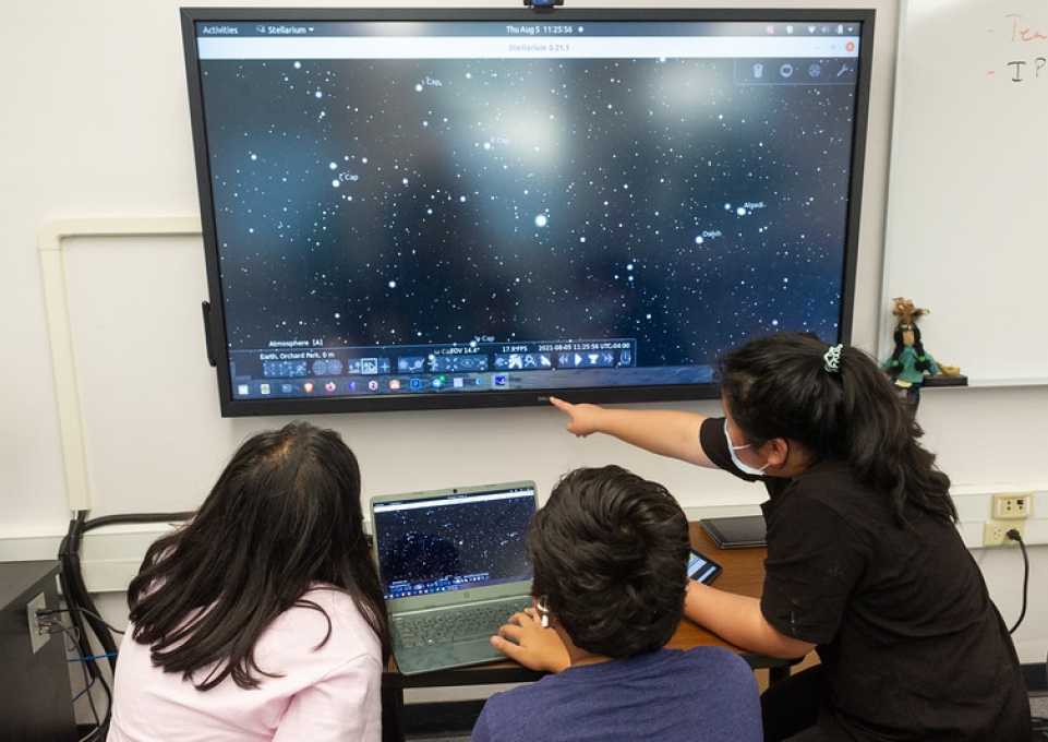 Three middle school students work with astronomy software on a large screen