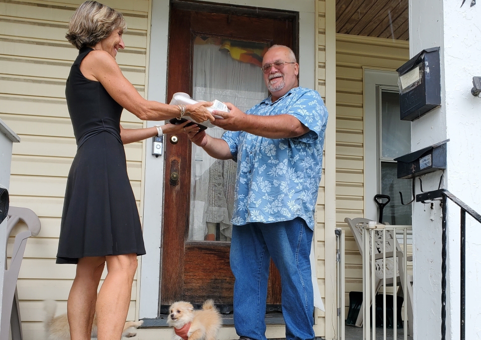 Carol DeNysschen handing a prepackaged meal to a client on his porch. 