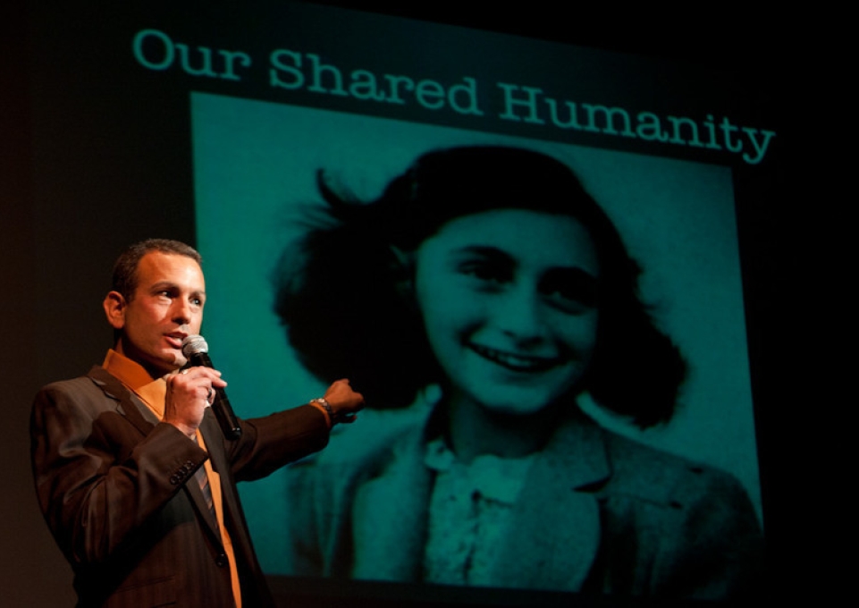 AFP director Drew Kahn standing in front of screen projection of Anne Frank and the words "Our Shared Humanity"