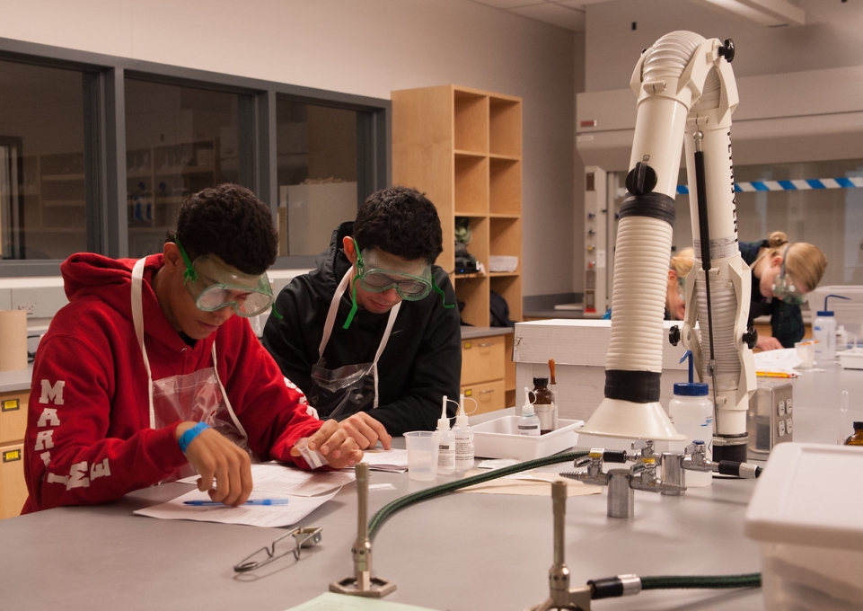 Two high school students wearing goggles and worokign together in a science lab