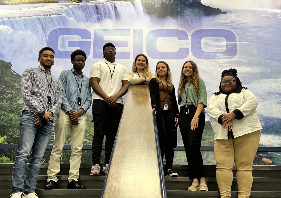 Students standing under a GEICO backdrop