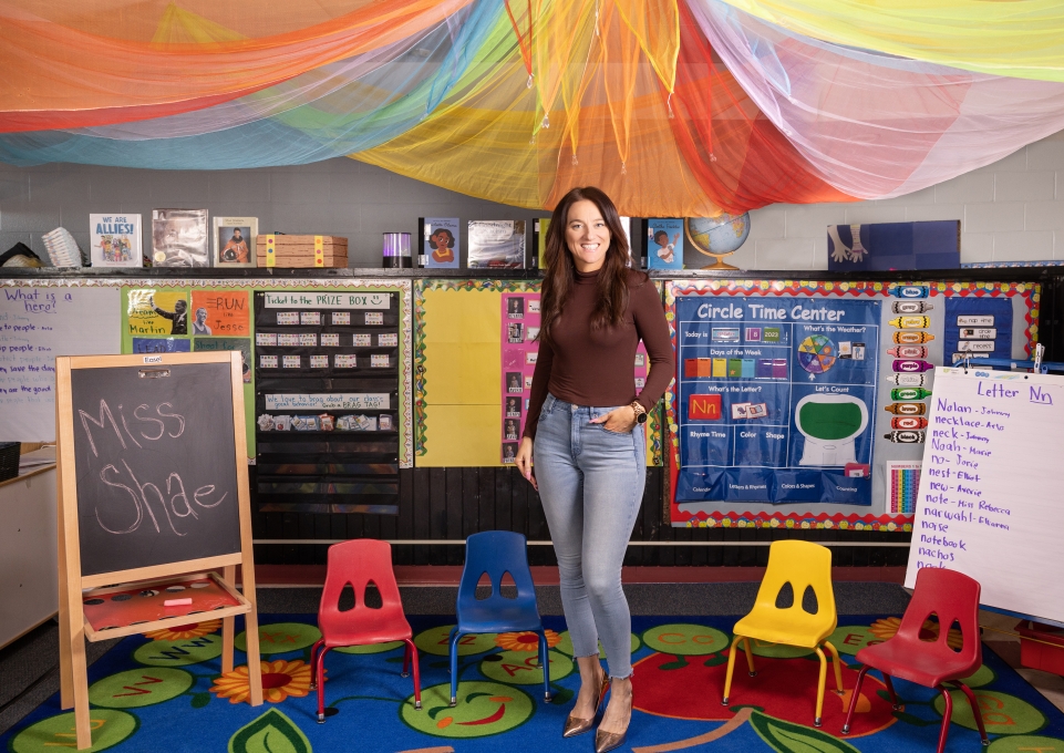 Shae Herron standing in her classroom surrounded by colorful chairs and educational supplies