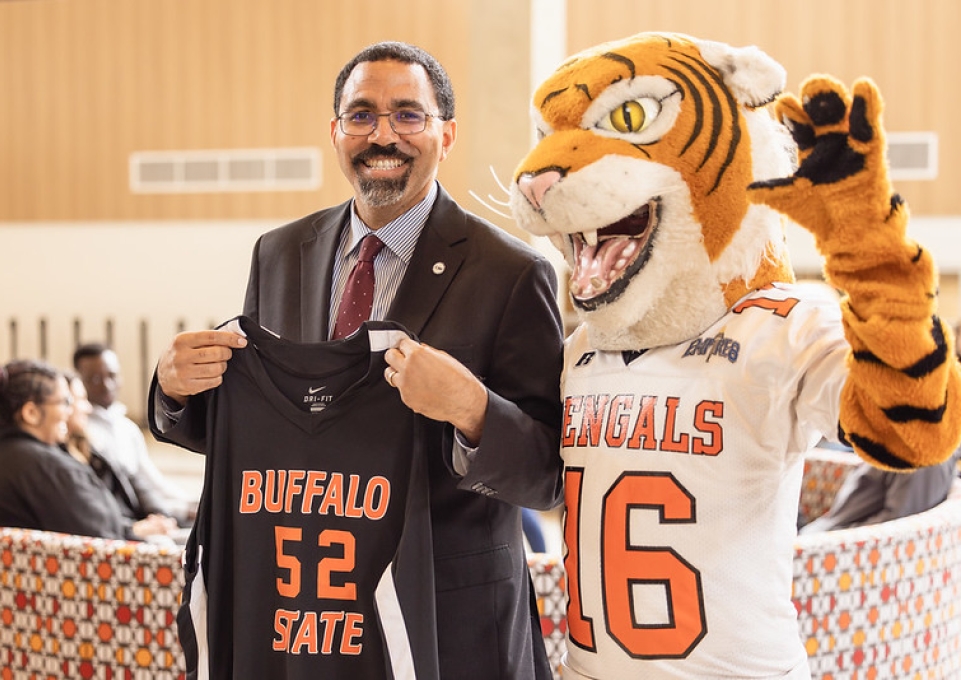 SUNY Chancellor John B. King holds a Buffalo State jersey and poses with mascot Benji