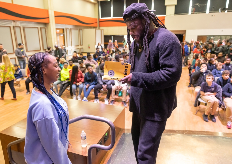 Jason Reynolds holds a copy of his book "Ghost" while talking to a middle school student