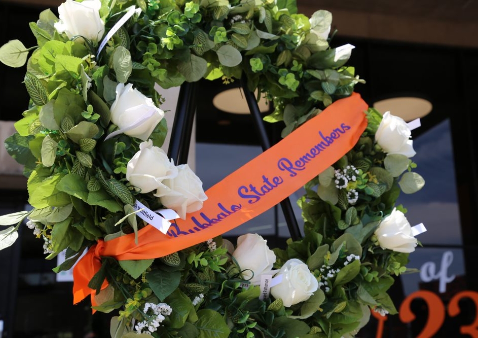 Wreath with white roses, the names of victims of the 5.14 massacre, and an orange ribbon that says Buffalo State Remembers