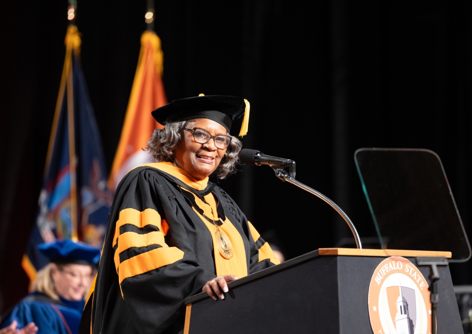 Bonita Durand stands at podium wearing regalia