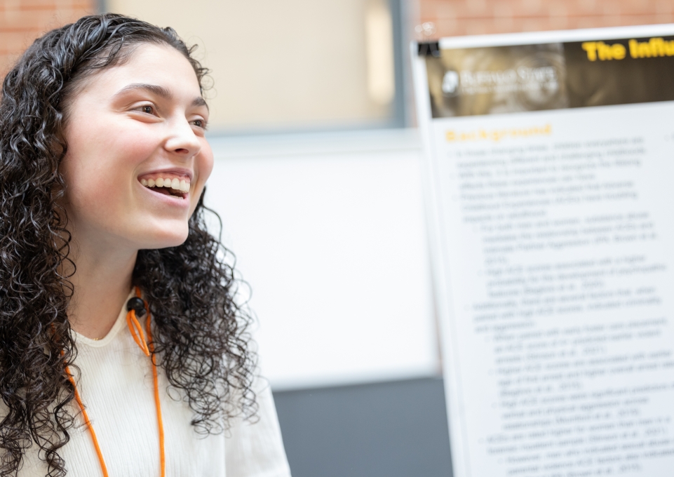 Student smiling standing in front of her research presentation poster