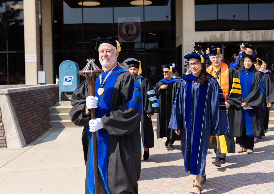 A group of faculty members process to Academic Convocation led by the mace bearer