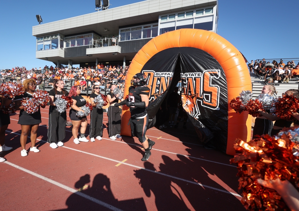 A football player bursts through a Bengal banner surrounded by cheerleaders